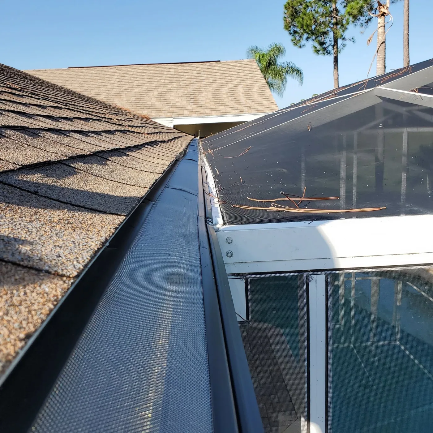 Fine black micro-mesh gutter guard along a roofline beside a screened pool enclosure