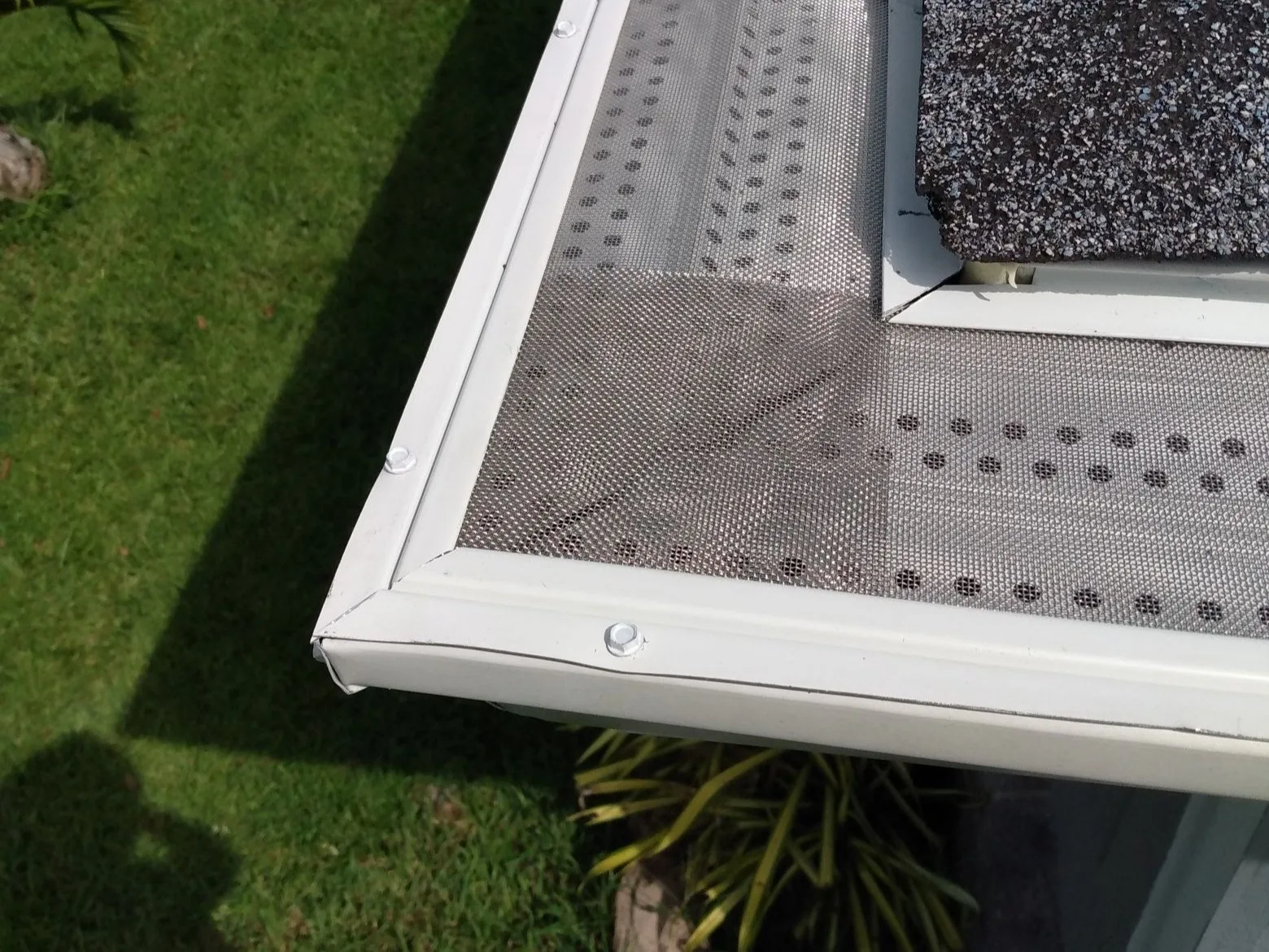 Close-up of ONE Gutter Guard stainless micro-mesh fitted at an outside gutter corner, the fine mesh keeping pine needles and leaves out of the gutter